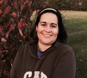 Author photograph, headshot of a Latinx woman with dark brown shoulder-length hair, wearing a brown sweatshirt