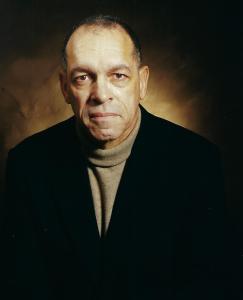James A. Scott author photo; white gentleman wearing a black blazer and tan turtleneck sweater in front of a dark brown background