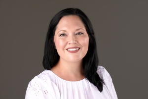 Emily Mayer author photo; a smiling white female with long, shoulder-length dark brown hair, wearing a white blouse